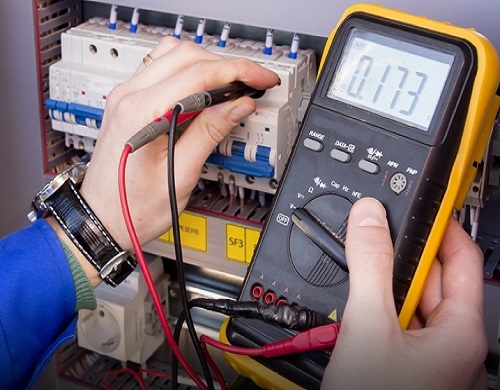 multimeter is in hands of engineer in electrical cabinet. Adjust